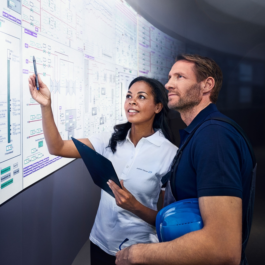 Dois engenheiros observam um amplo display em uma sala de controle industrial.