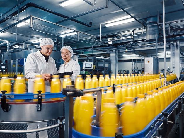 Dois engenheiros em uma fábrica de bebidas supervisionando o processo de envase de suco de laranja.