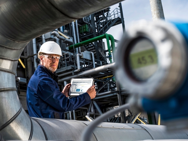 Engenheiro trabalhando em um tablet industrial em um ambiente de refinaria.