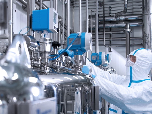 Engenheiro em traje sanitário operando um equipamento em ambiente de life sciences.