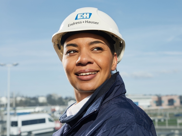 Engenheira com capacete branco em frente ao céu azul.